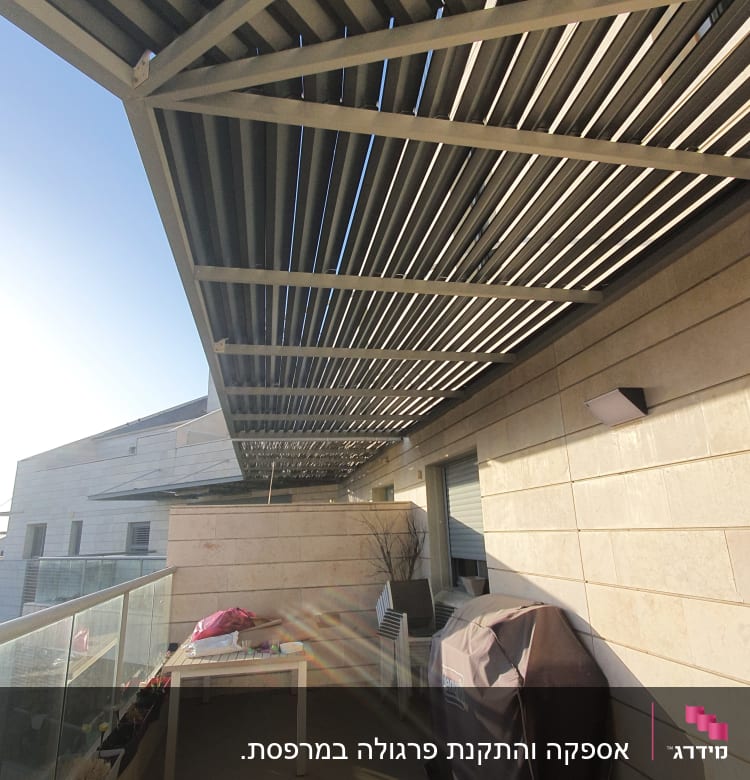 פרגולה מתכתית מעל מרפסת עם שולחן וכיסוי גריל